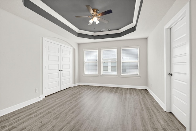 unfurnished bedroom featuring a tray ceiling, baseboards, visible vents, and wood finished floors