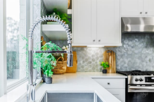 kitchen featuring stainless steel gas range oven, a healthy amount of sunlight, wall chimney range hood, and white cabinets