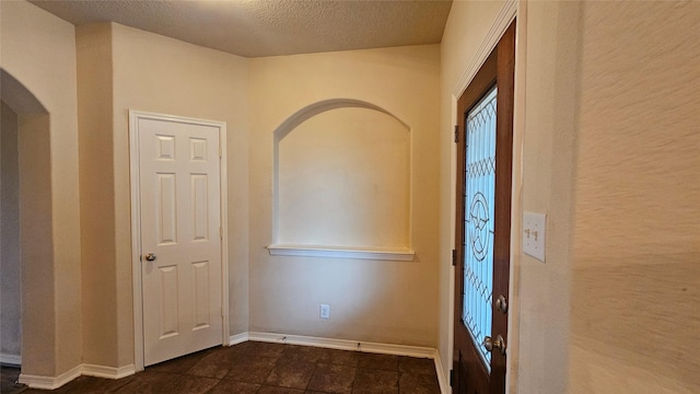 entrance foyer with baseboards, arched walkways, and a textured ceiling