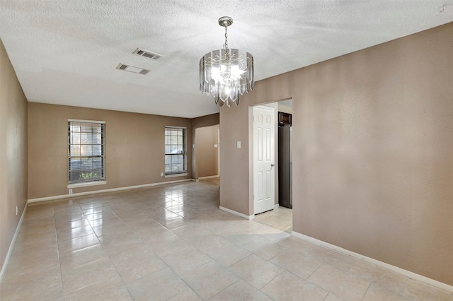 tiled empty room featuring a notable chandelier and a textured ceiling