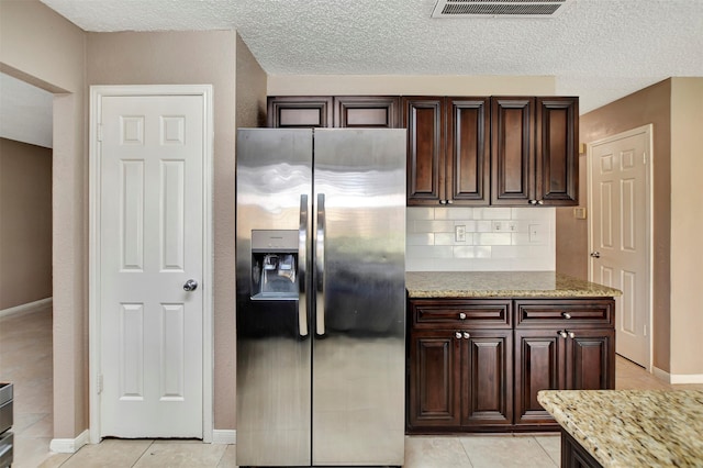 kitchen with dark brown cabinetry, light stone counters, stainless steel fridge with ice dispenser, light tile patterned floors, and backsplash