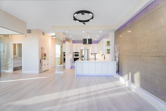 kitchen featuring appliances with stainless steel finishes, white cabinetry, sink, light hardwood / wood-style floors, and kitchen peninsula