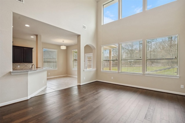 unfurnished living room with recessed lighting, visible vents, a sink, wood finished floors, and baseboards