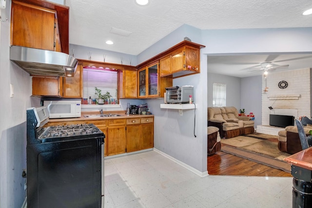 kitchen with sink, ceiling fan, a fireplace, stainless steel range with gas cooktop, and exhaust hood