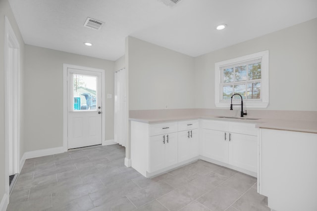 kitchen with baseboards, visible vents, light countertops, white cabinetry, and a sink