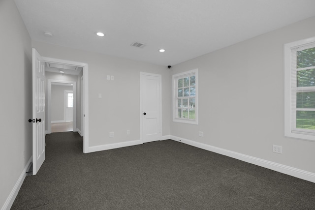 empty room featuring dark colored carpet, attic access, and a healthy amount of sunlight