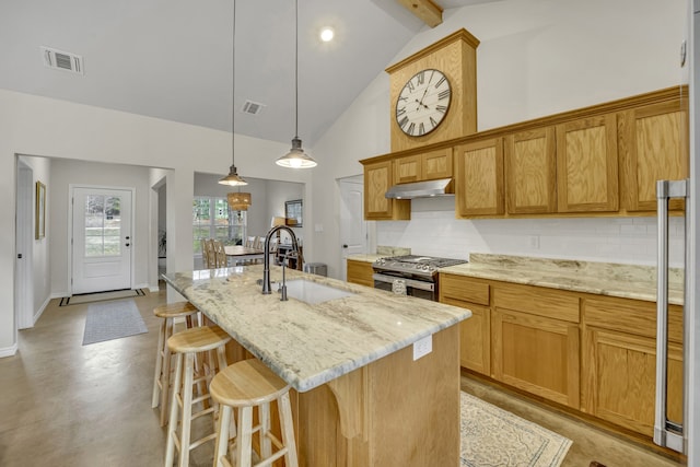 kitchen with pendant lighting, sink, stainless steel gas range, high vaulted ceiling, and an island with sink