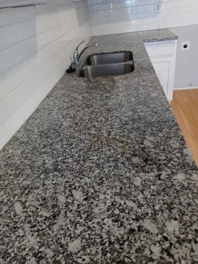 room details with sink, decorative backsplash, white cabinets, and hardwood / wood-style flooring