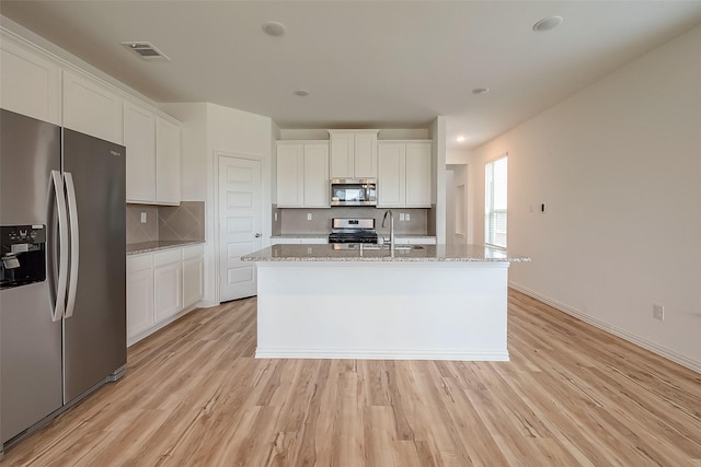 kitchen featuring white cabinetry, light stone counters, stainless steel appliances, and an island with sink