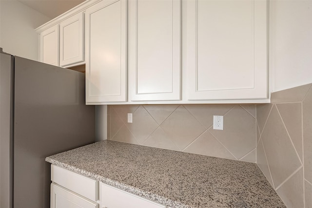 kitchen featuring light stone counters, backsplash, stainless steel refrigerator, and white cabinets