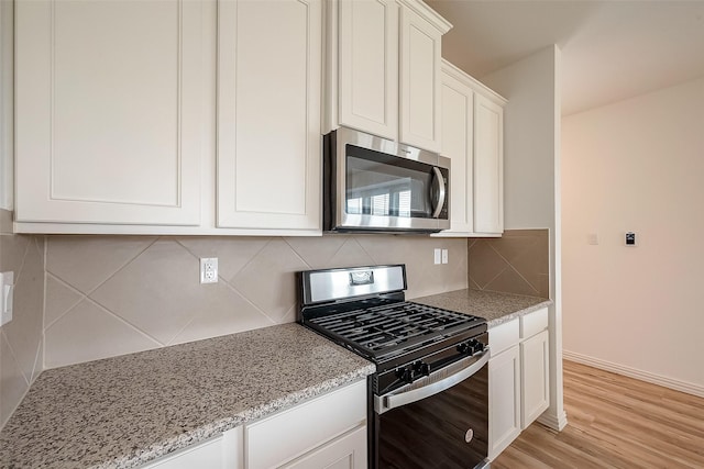 kitchen with white cabinets, decorative backsplash, light stone counters, light hardwood / wood-style floors, and gas range oven