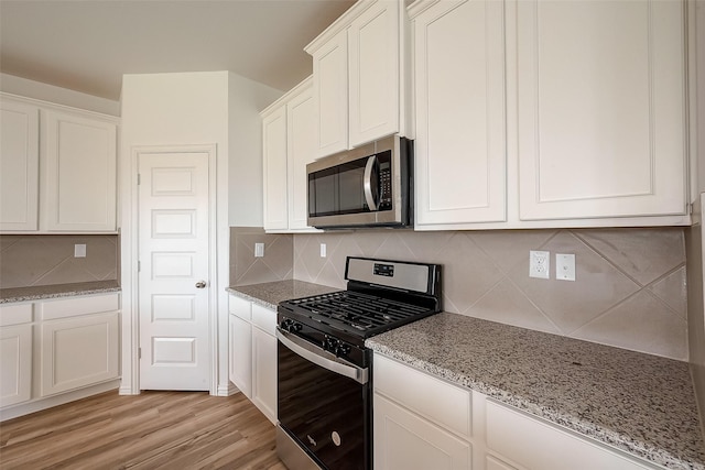 kitchen with white cabinetry, backsplash, light stone countertops, and appliances with stainless steel finishes