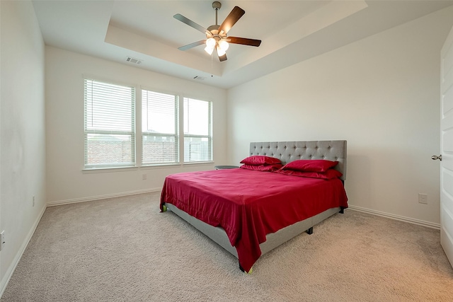 bedroom with light colored carpet, ceiling fan, and a tray ceiling