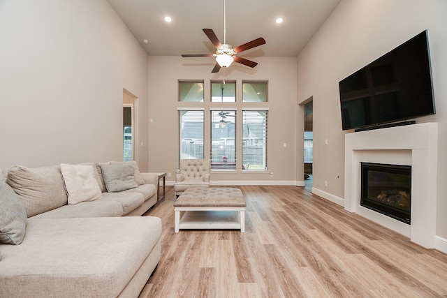 living room with ceiling fan, light hardwood / wood-style flooring, and a towering ceiling