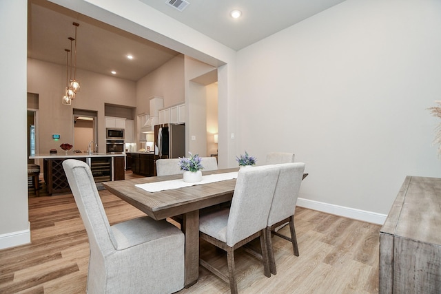 dining area featuring a towering ceiling, beverage cooler, and light hardwood / wood-style floors