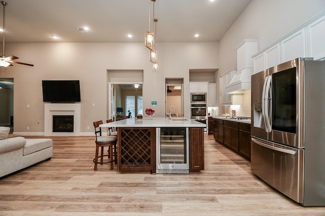 kitchen with wine cooler, sink, hanging light fixtures, a center island with sink, and stainless steel appliances