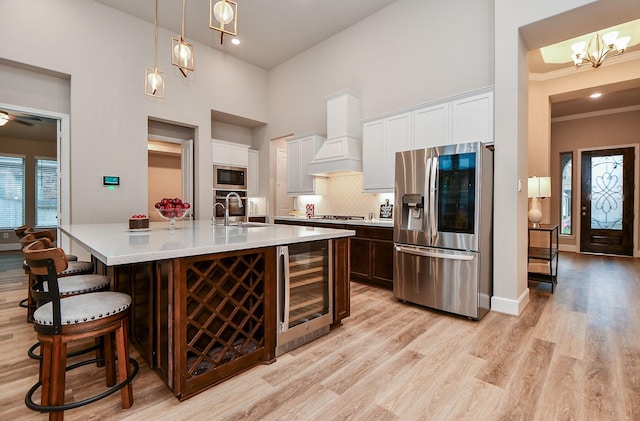 kitchen with wine cooler, an island with sink, pendant lighting, stainless steel appliances, and white cabinets