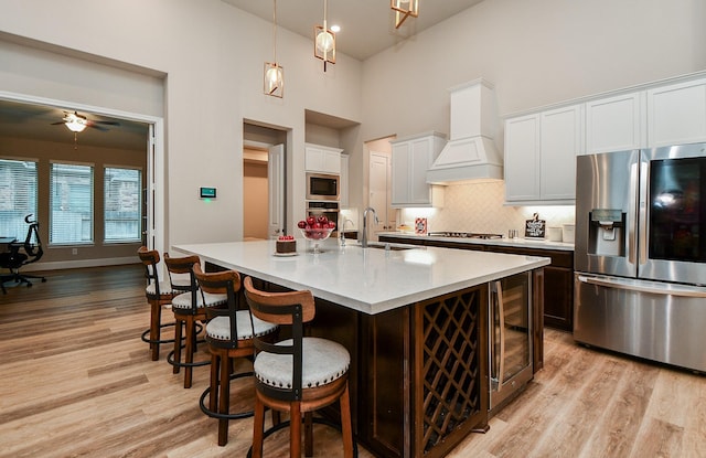 kitchen featuring appliances with stainless steel finishes, sink, white cabinets, custom exhaust hood, and a kitchen island with sink