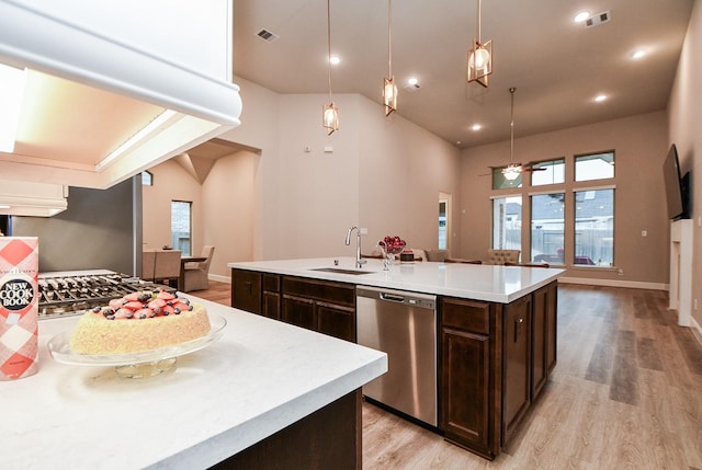 kitchen with decorative light fixtures, an island with sink, sink, stainless steel dishwasher, and light wood-type flooring