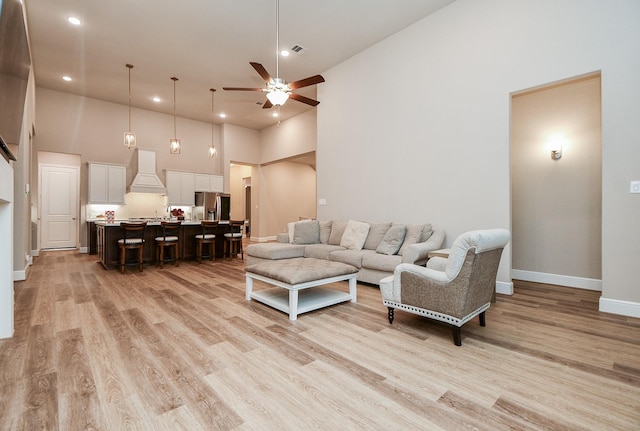 living room featuring ceiling fan, a towering ceiling, and light hardwood / wood-style flooring