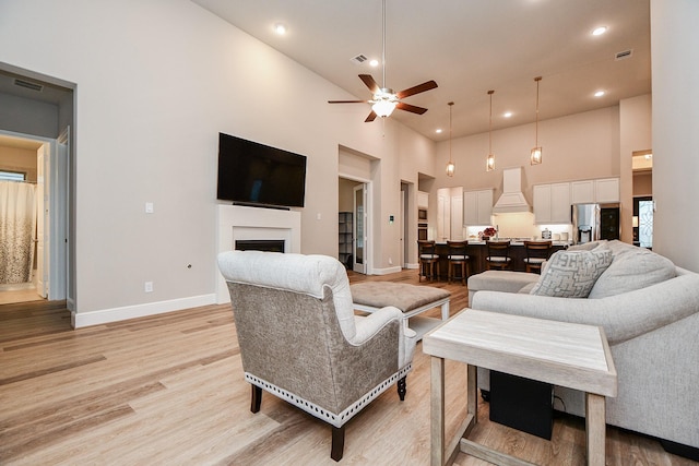 living room with ceiling fan, a towering ceiling, and light hardwood / wood-style floors