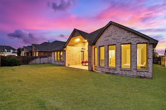 back house at dusk featuring a lawn and a patio