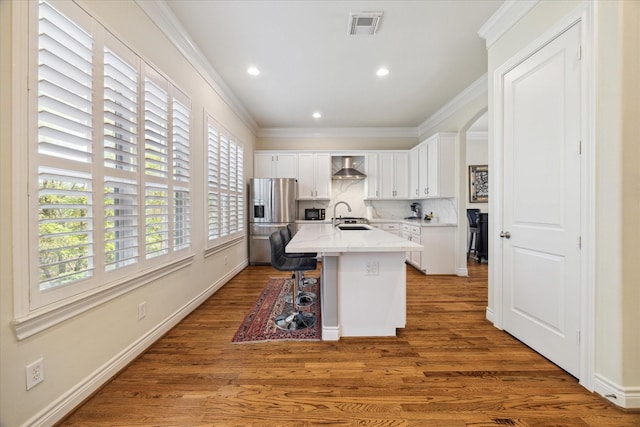 kitchen featuring white cabinets, a kitchen bar, ornamental molding, a kitchen island with sink, and stainless steel refrigerator with ice dispenser