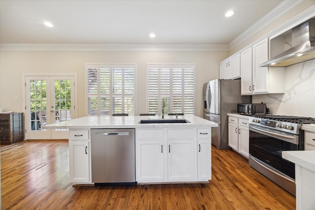 kitchen featuring appliances with stainless steel finishes, white cabinetry, an island with sink, sink, and wall chimney range hood