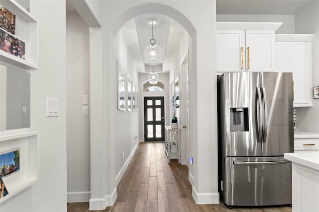 kitchen with light hardwood / wood-style flooring, hanging light fixtures, stainless steel fridge, and white cabinets