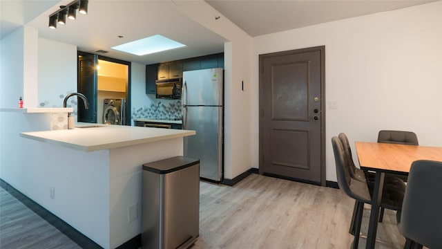 kitchen with sink, stainless steel refrigerator, light hardwood / wood-style floors, washer / clothes dryer, and kitchen peninsula