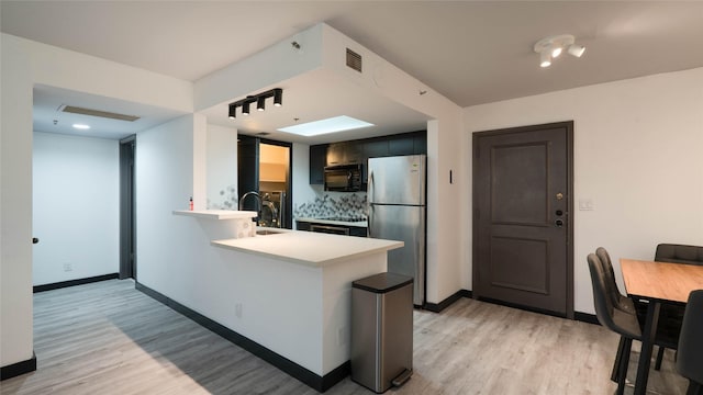 kitchen with sink, tasteful backsplash, appliances with stainless steel finishes, kitchen peninsula, and light hardwood / wood-style floors