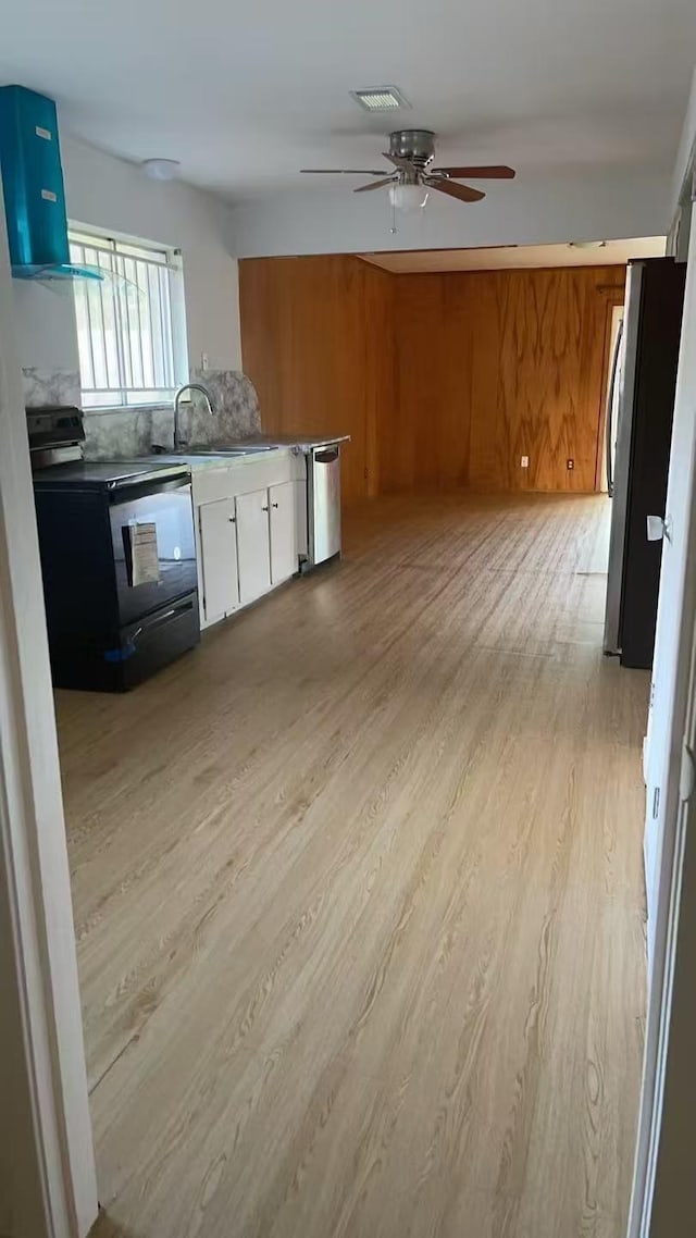 kitchen with sink, light wood-type flooring, exhaust hood, wood walls, and stainless steel appliances