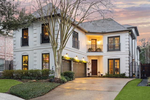 view of front facade featuring an attached garage, a balcony, driveway, a gate, and stucco siding