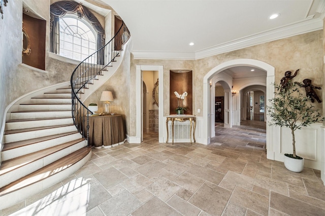 entrance foyer featuring crown molding, stairs, arched walkways, and stone tile flooring