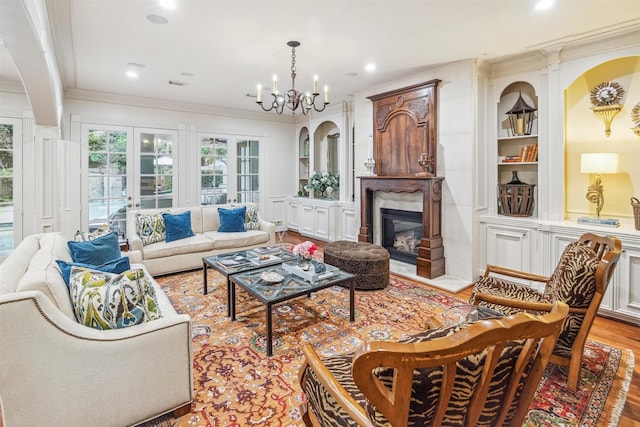 living room with a chandelier, crown molding, built in shelves, light wood-type flooring, and french doors