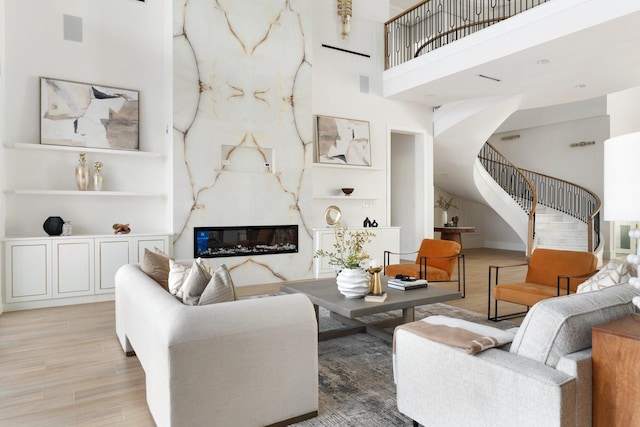 living room with a fireplace, visible vents, a towering ceiling, wood finished floors, and stairs