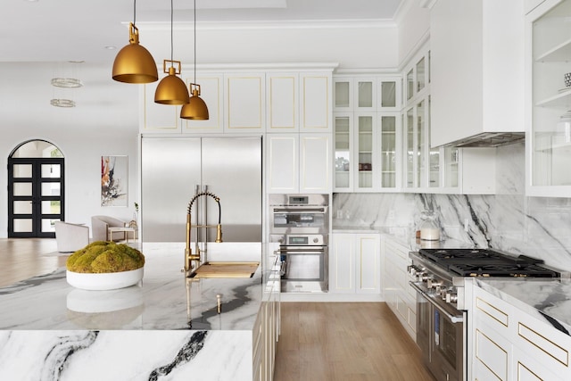 kitchen featuring premium appliances, light stone counters, decorative light fixtures, tasteful backsplash, and white cabinets