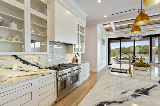 kitchen with light wood finished floors, coffered ceiling, light stone counters, double oven range, and backsplash