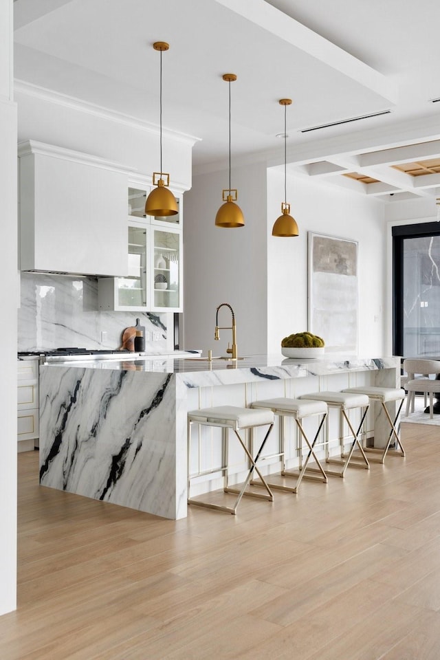 kitchen with light wood-style floors, a kitchen bar, decorative backsplash, and light stone countertops