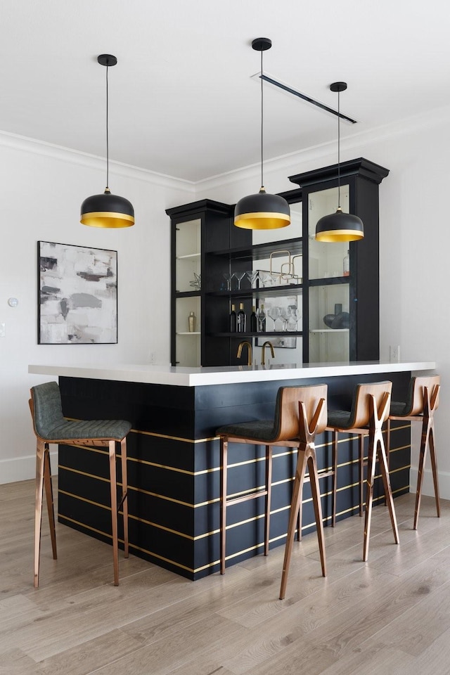 bar with hanging light fixtures, light wood-style floors, indoor wet bar, and crown molding