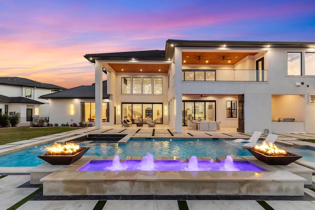 back of house at dusk featuring a fire pit and stucco siding