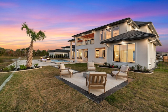 back of house at dusk with a patio, a yard, a balcony, and stucco siding