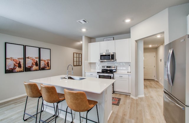 kitchen featuring appliances with stainless steel finishes, white cabinetry, sink, a kitchen breakfast bar, and a kitchen island with sink