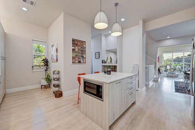 kitchen featuring pendant lighting, light hardwood / wood-style floors, a kitchen island, and black microwave