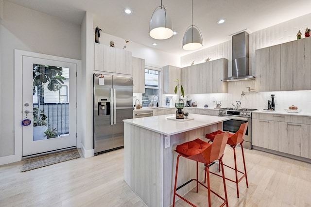 kitchen featuring a kitchen island, a breakfast bar, decorative light fixtures, stainless steel appliances, and wall chimney range hood