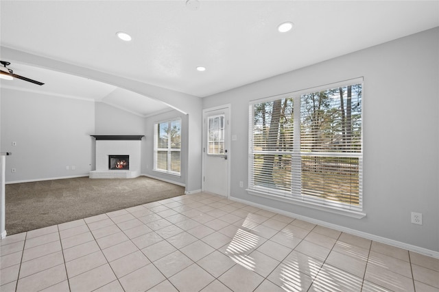 unfurnished living room featuring arched walkways, lofted ceiling, carpet flooring, a warm lit fireplace, and tile patterned floors