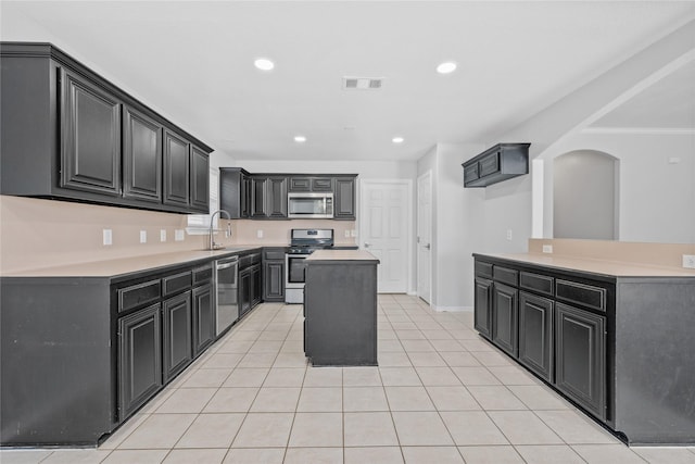 kitchen featuring light tile patterned floors, visible vents, dark cabinets, a center island, and stainless steel appliances