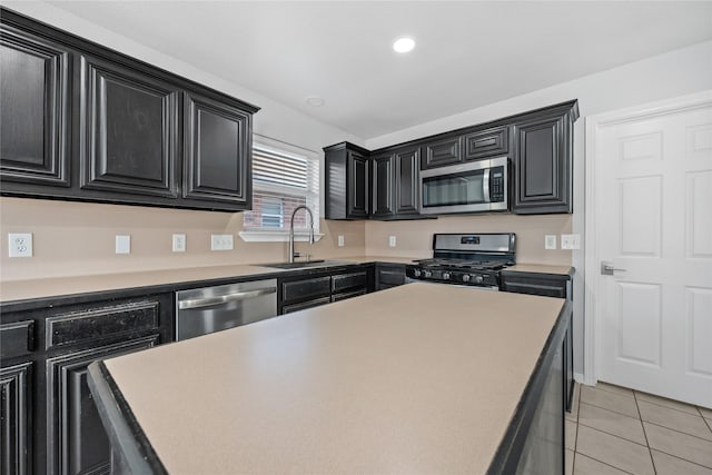 kitchen featuring dark cabinetry, appliances with stainless steel finishes, a sink, and light tile patterned flooring