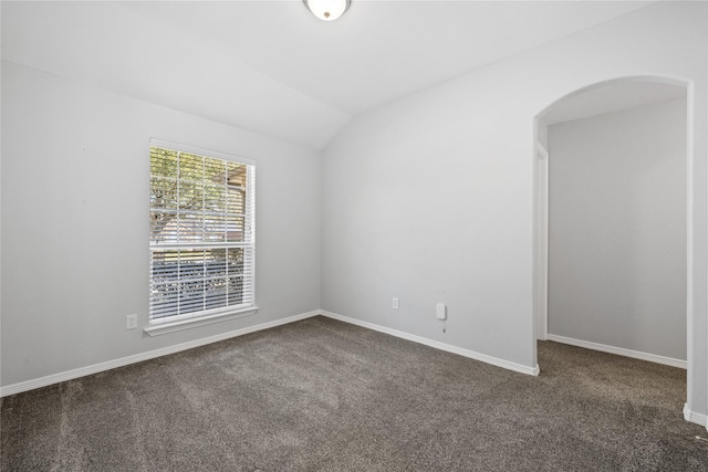 spare room with lofted ceiling, baseboards, dark carpet, and arched walkways