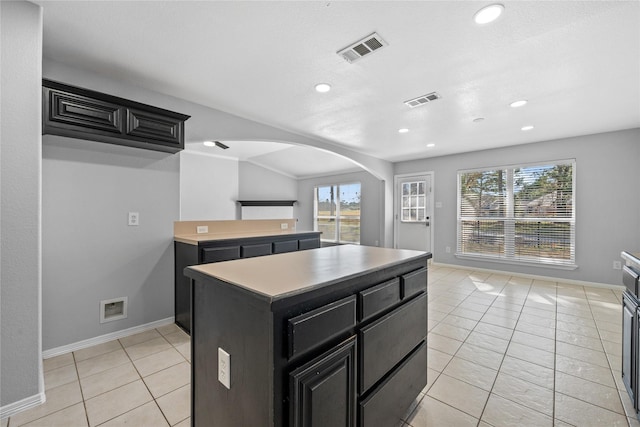 kitchen with dark cabinets, arched walkways, visible vents, and a kitchen island